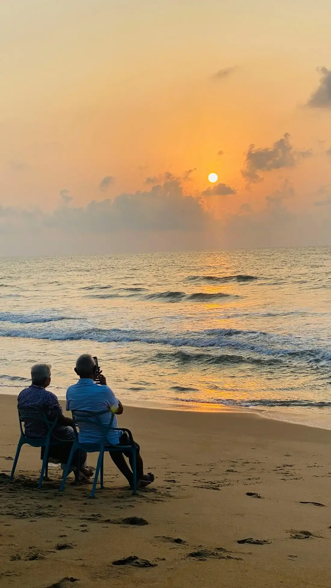 Senior couple sitting together on a beach watching a golden sunset