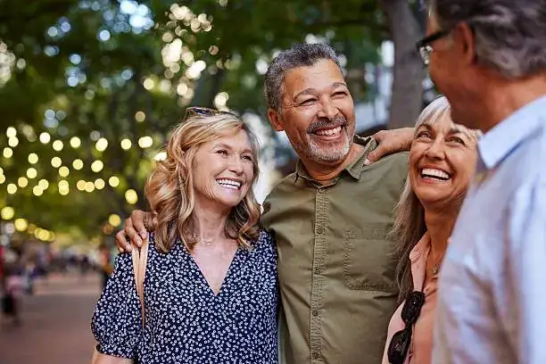 Group of mature friends laughing together outdoors under string lights